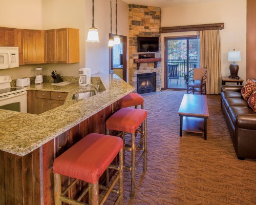 AN OPEN PLAN LIVING AND KITCHEN AREA WITH A TELEVISION FIREPLACE AND BREAKFAST BAR.