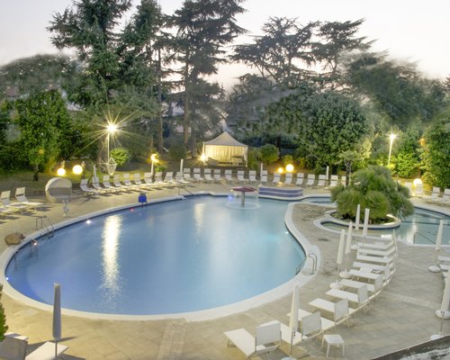 An outdoor swimming pool with chaise lounge chairs at dusk.