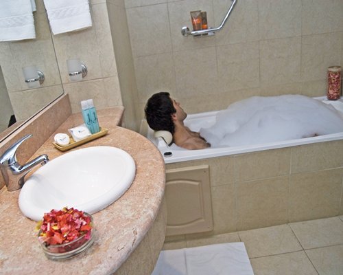 A man inside the bathtub at a bathroom with shower and sink.