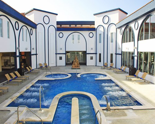 An outdoor spa pool with chaise lounge chairs surrounded by building exterior.