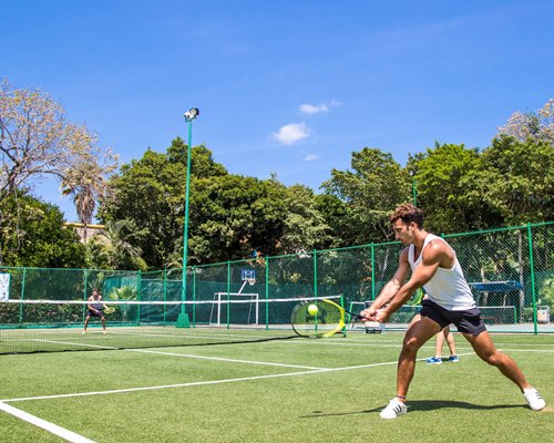 An outdoor turf tennis court with people playing doubles.