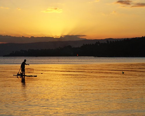 A man fishing in the waterfront at sunset.