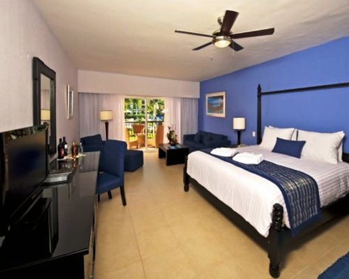 A well furnished bedroom with a king bed television and balcony.