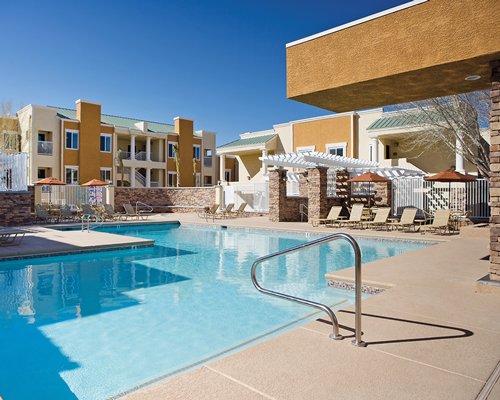 An outdoor swimming pool with chaise lounge chairs and sunshades alongside resort units.