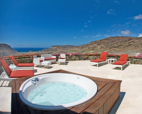 An outdoor hot tub with chaise lounge chairs and patio alongside the mountains.
