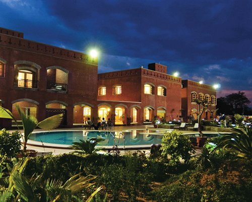 An outdoor swimming pool with chaise lounge chairs alongside multi story resort units at night.