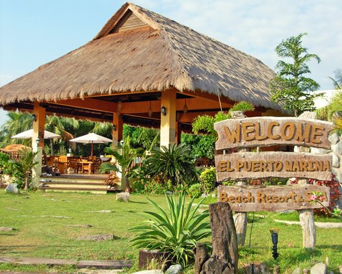 Signboard of El Puerto Marina Beach Resort alongside gazebo with a thatched roof.