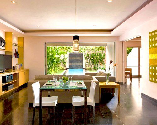 An open plan living and glass top dining area with a television and an outside view.