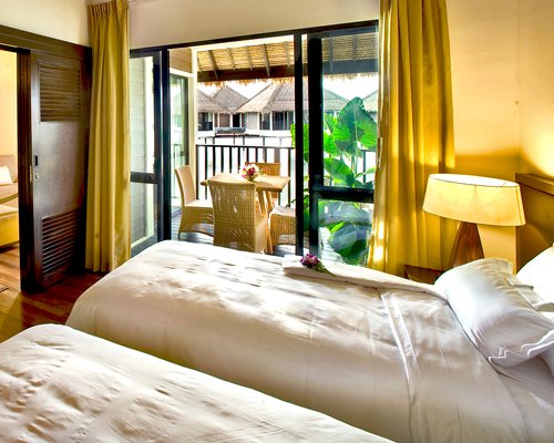 A well furnished bedroom with two twin beds and a balcony with patio furniture.