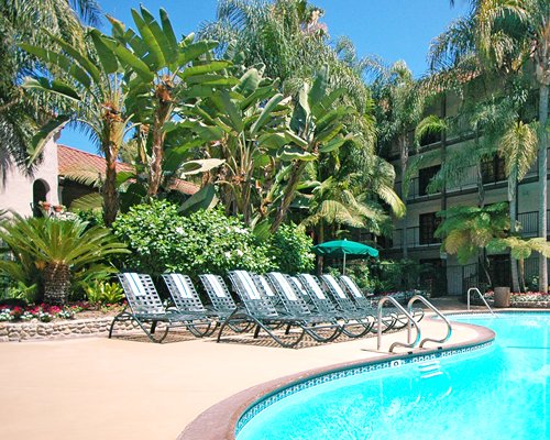 An outdoor swimming pool with chaise lounge chairs and trees alongside multi story resort units.