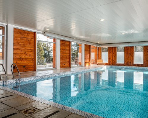 An indoor swimming pool with chaise lounge chairs and an outside view.