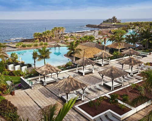 Large outdoor swimming pool with covered beach beds alongside the ocean.