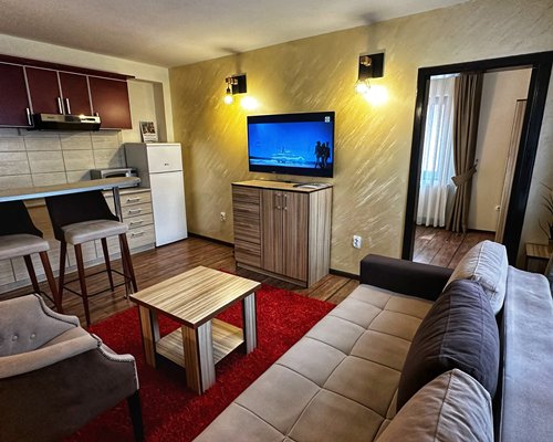 An open plan living area with a television alongside the kitchen with a breakfast bar.
