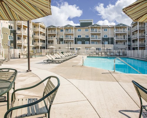 VIEW OF MULTIPLE UNIT BALCONIES ALONGSIDE SWIMMING POOL WITH CHAISE LOUNGE CHAIRS.