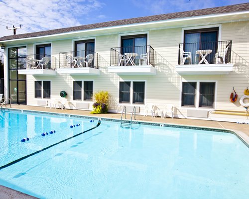 An outdoor swimming pool with patio furniture alongside multi story unit with private balconies.