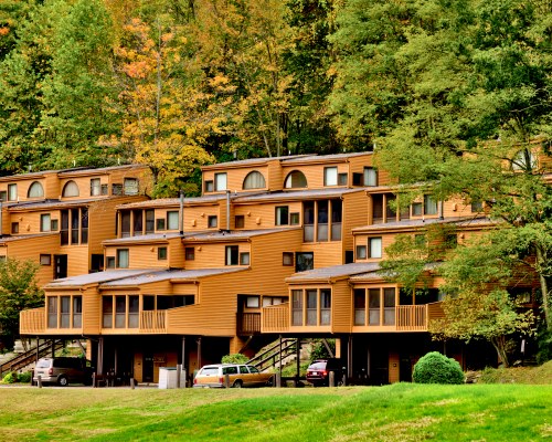 AN EXTERIOR VIEW OF MULTI STORY RESORT UNITS WITH A PARKING LOT AND TREES.