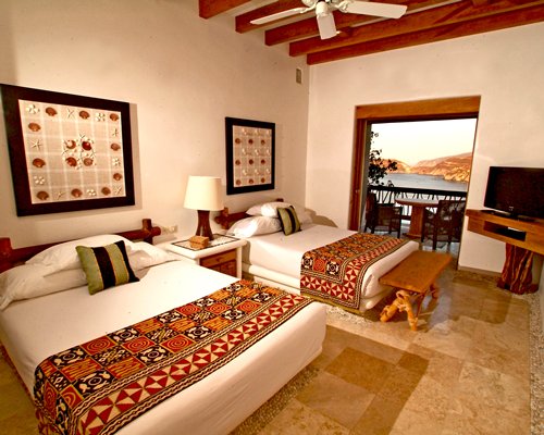 A well furnished bedroom with two beds a television and balcony.