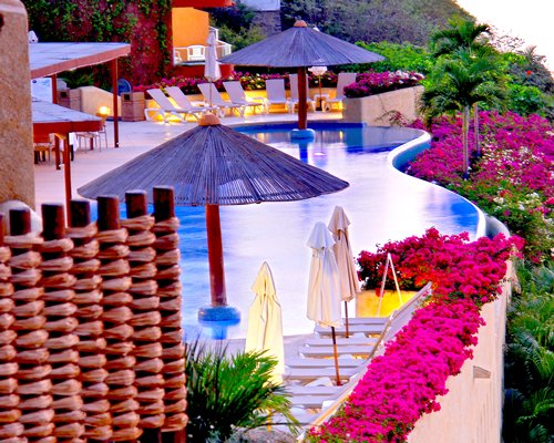 An outdoor swimming pool with chaise lounge chairs and sunshades.
