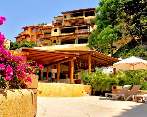 An exterior view of multi story resort units with chaise lounge chairs trees and flowering shrubs.