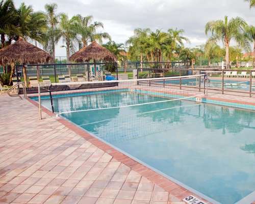 A scenic outdoor swimming pool with a volleyball setup chaise lounge chairs and sunshades.