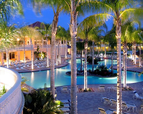 An outdoor swimming pool with chaise lounge chairs surrounded by palm trees alongside resort units.