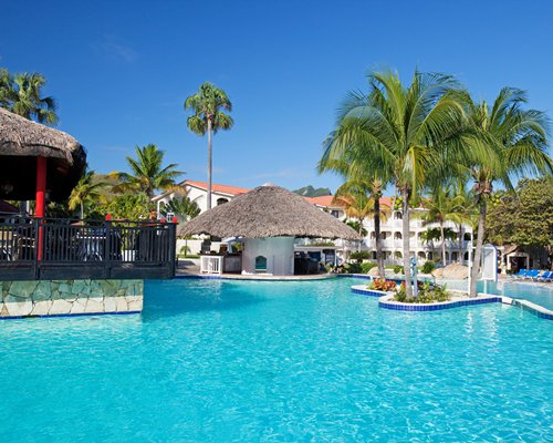 Large outdoor swimming pool with thatched covered poolside bar and chaise lounge chairs.