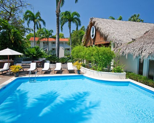An outdoor swimming pool with chaise lounge chairs and sunshade alongside a pool bar.