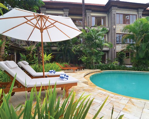 A scenic outdoor swimming pool with chaise lounge chairs and sunshade alongside multi story units.