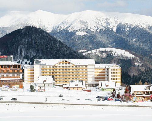 An exterior view of multi story resort units covered in snow alongside mountains.