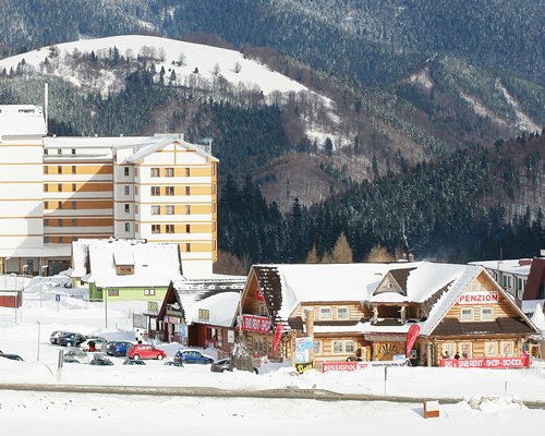 Exterior view of Residence Club with parking lot alongside the mountains and wooded area during winter.