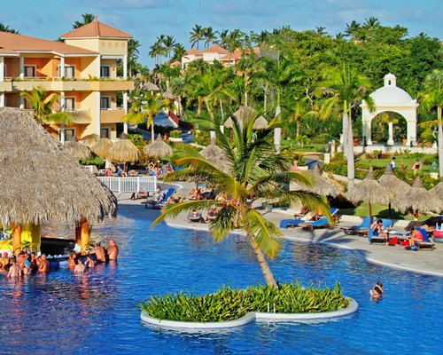 An outdoor pool with a swim up bar chaise lounge chairs and thatched sunshades alongside the resort.