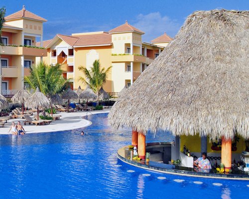 An outdoor swimming pool with chaise lounge chairs thatched sunshades and swim up pool bar.