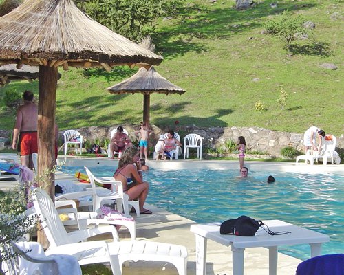 An outdoor pool with thatched sunshades chaise lounge chairs and patio furniture alongside the lawn.