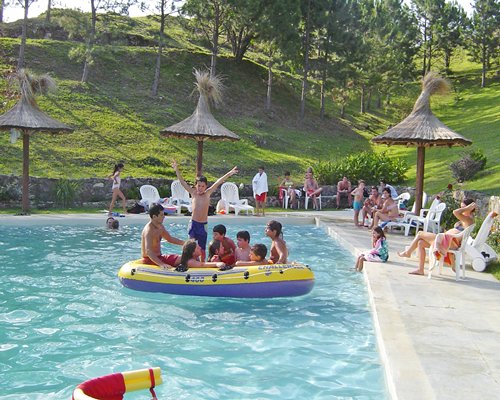 Group of people in the pool floats of an outdoor swimming pool with chaise lounge chairs and patio furniture.