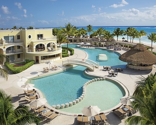 A bridge over a large outdoor swimming pool alongside and the beach.