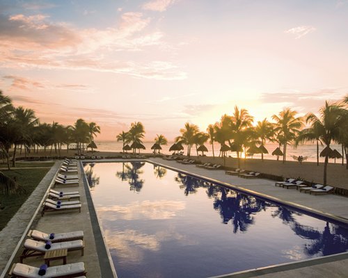 A large outdoor swimming pool with chaise lounge chairs at dusk.