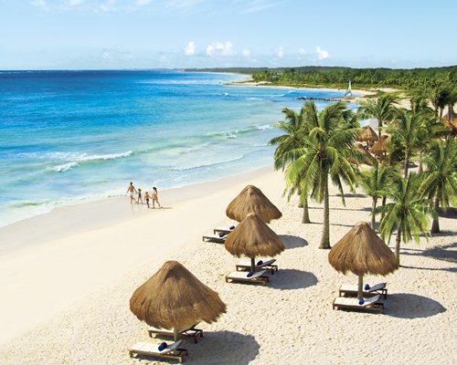 View of the beach with thatched sunshades and chaise lounge chairs.