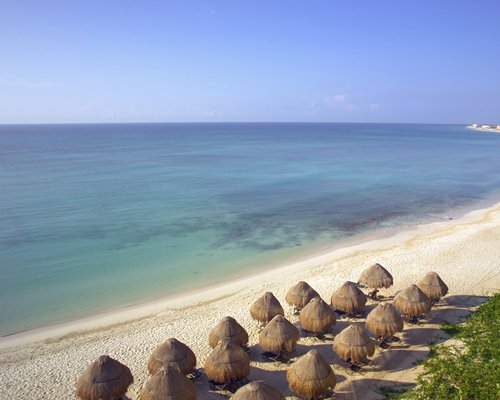 View of the beach with chaise lounge chairs and thatched sunshades alongside the ocean.