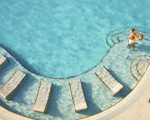 An aerial view of a couple in the outdoor swimming pool with in pool chaise lounge chairs.