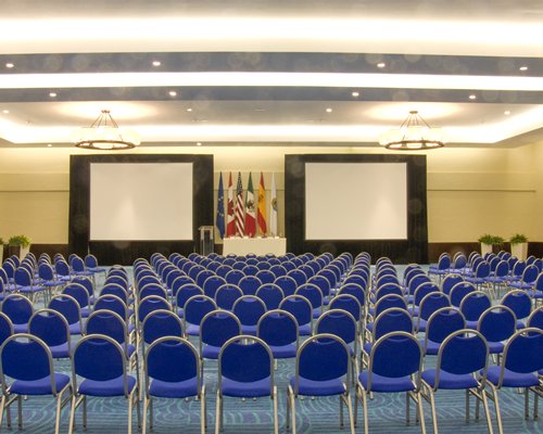 An interior view of a well furnished conference hall with two projection screens.