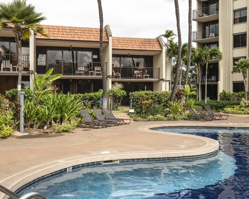 A scenic outdoor swimming pool with chaise lounge chairs and trees alongside multi story units.