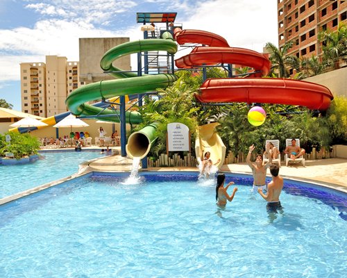 A group of people enjoying an outdoor swimming pool with water slides alongside multi story resort units.