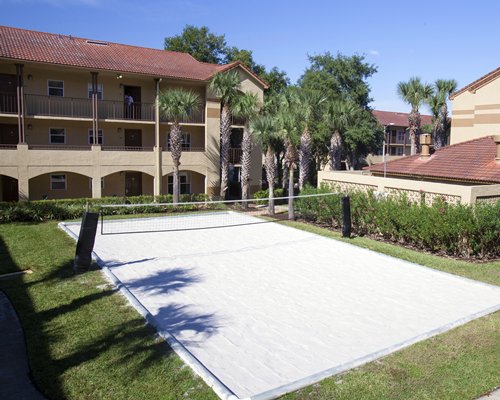 An outdoor tennis court with palm trees and shrubs alongside multi story resort units.