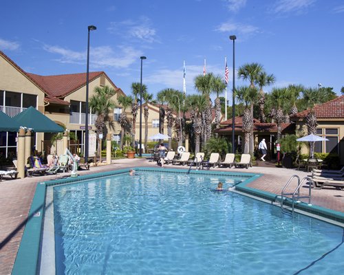 An outdoor swimming pool with chaise lounge chairs and palm trees alongside multi story resort units.