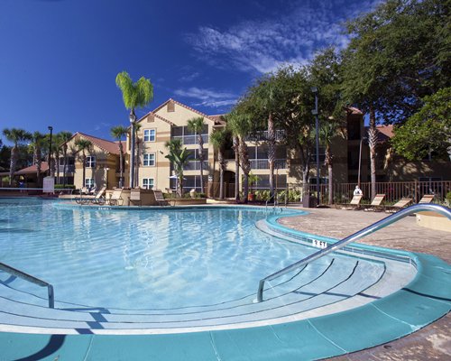 An outdoor swimming pool with chaise lounge chairs alongside resort units and trees.