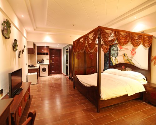 A well furnished bedroom with a television and kitchen.