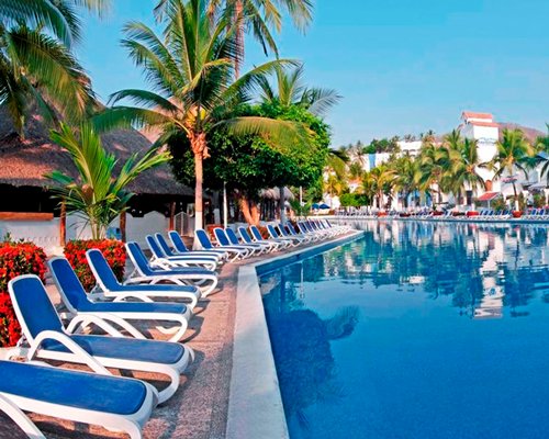 A large outdoor swimming pool with chaise lounge chairs and trees alongside resort units.