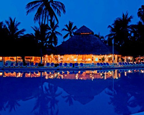 Night view of an outdoor pool with chaise lounge chairs alongside a snack bar.