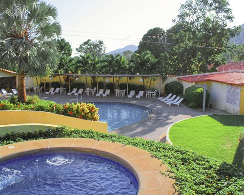 An outdoor hot tub and swimming pool with chaise lounge chairs and landscaping.