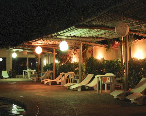 View of chaise lounge chairs alongside the pool at night.